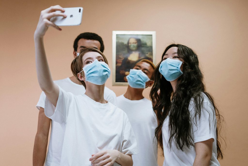 A group of young people wearing masks takes a selfie indoors, with a Mona Lisa painting in the background.